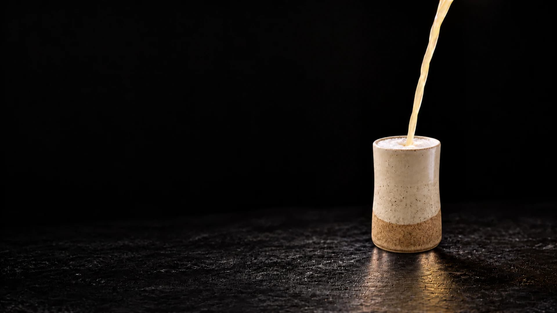 Lúmine Sour cayendo en un vaso de cerámica artesanal, sobre fondo negro